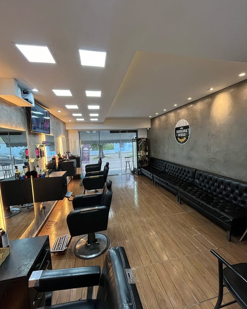 Salão da Barbearia Murilo em Santa Bárbara, Niterói — vista interna com lounge e o emblema da casa na parede